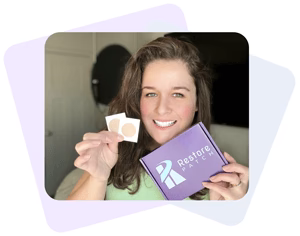 A woman is holding two Restore patches on her right hand and a Restore Patch Migraine-Headache Patch box on her left hand.