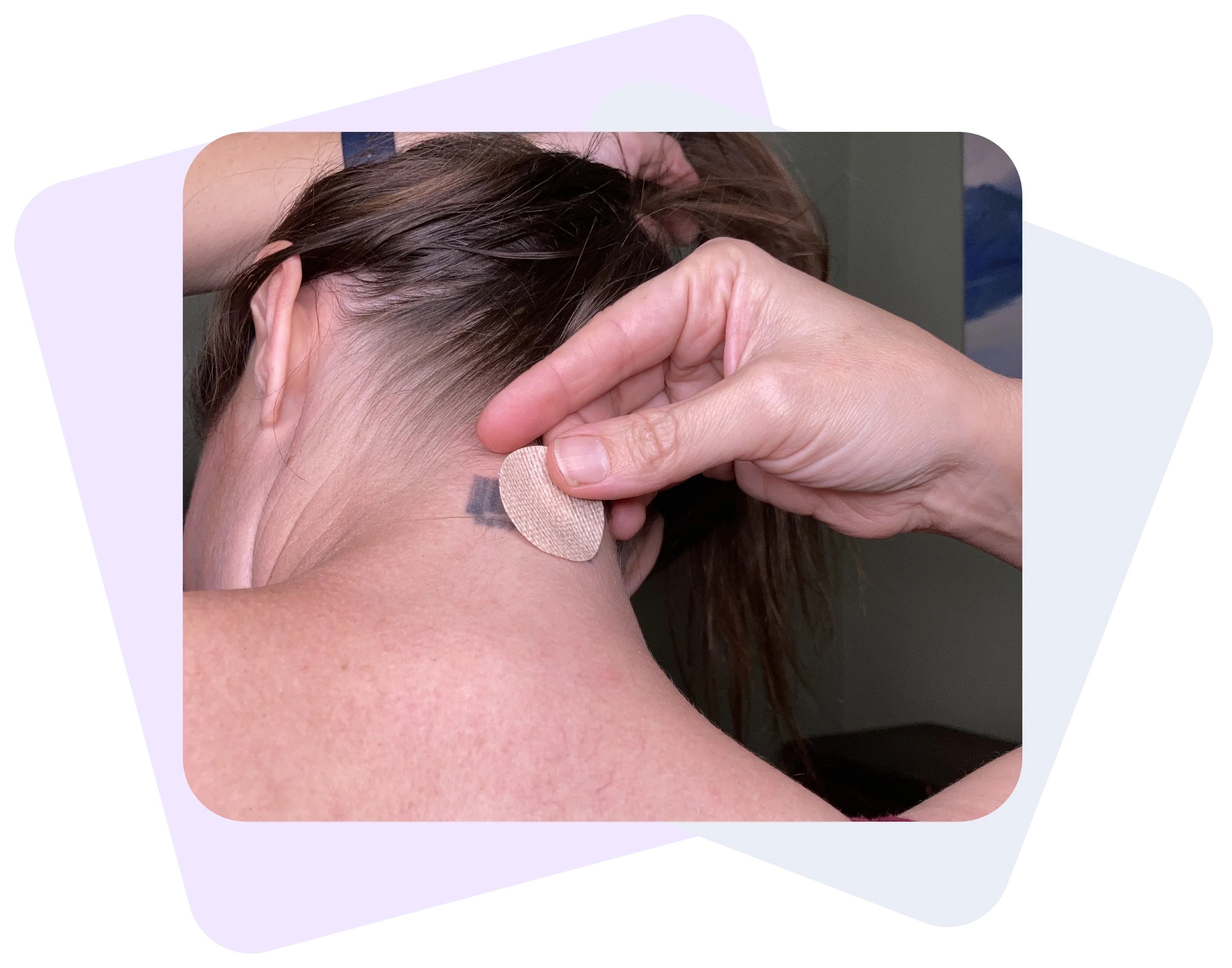 A woman facing backwards with her head slightly tilted down is holding her hair as she tries to put a Restore patch on her nape, covering her tattoo.