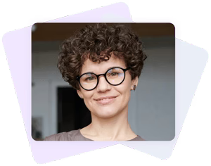 An image of a woman with a curly hair wearing eyeglasses is smiling.