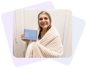 A smiling woman with a blanket wrapped around her is holding a box of Restore Patch Sleep Patch.
