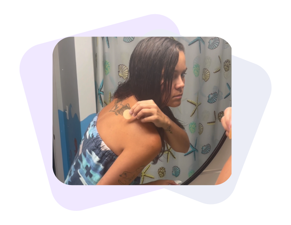 A woman is looking at the mirror while applying a Restore patch on her left shoulder.