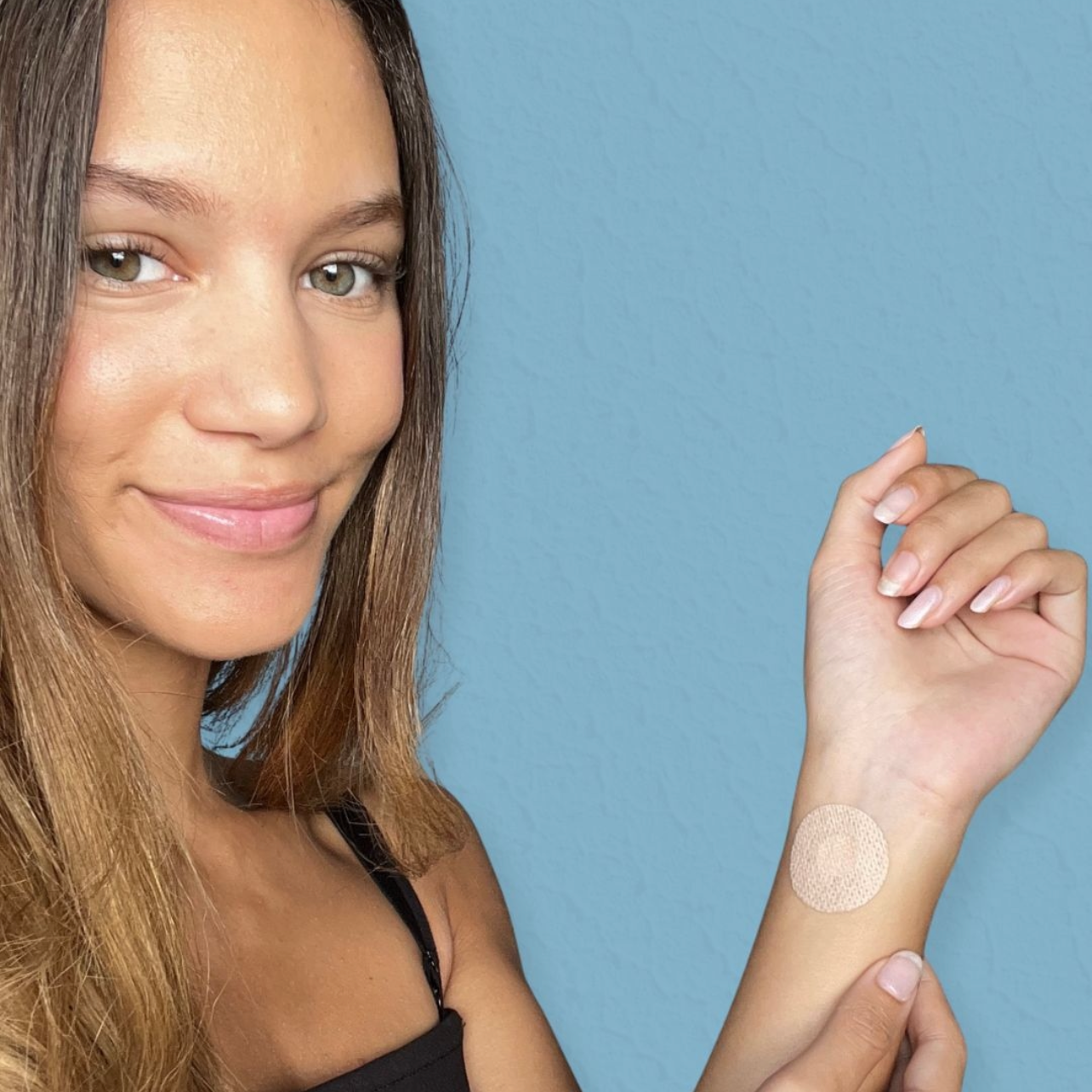 A girl smiling while showing the energy patch she applied on her wrist