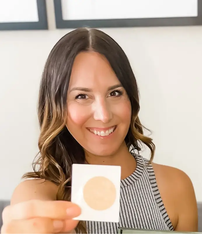 A smiling woman is wearing a striped tank top while holding and showing a Restore patch.